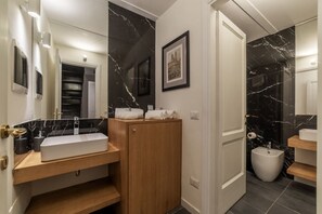 Ett modernt badrum med en vit tvättställ, ett träfärgat handfatsskåp och väggar klädda i svart marmor.