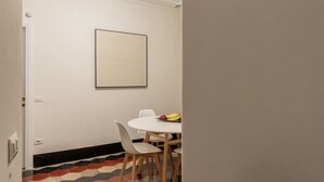 A dining area with a white table and chairs, a framed artwork on the wall, and a fruit bowl on the table.
