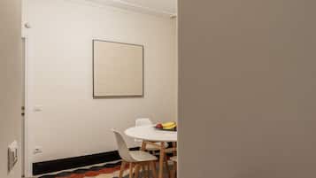 A dining area with a white table and chairs, a framed artwork on the wall, and a fruit bowl on the table.