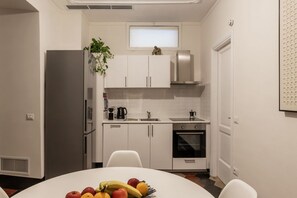A modern kitchen with white cabinets, a stainless steel refrigerator, a microwave, and an oven. There is a plant on the countertop and a fruit bowl on the table. - La dolce vita is around the corner (Roma)