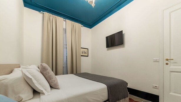 A bedroom with a bed, a television on the wall, a door, and a window with curtains.