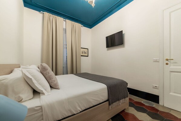 A bedroom with a bed, a television on the wall, a door, and a window with curtains. - La dolce vita is around the corner (Roma)