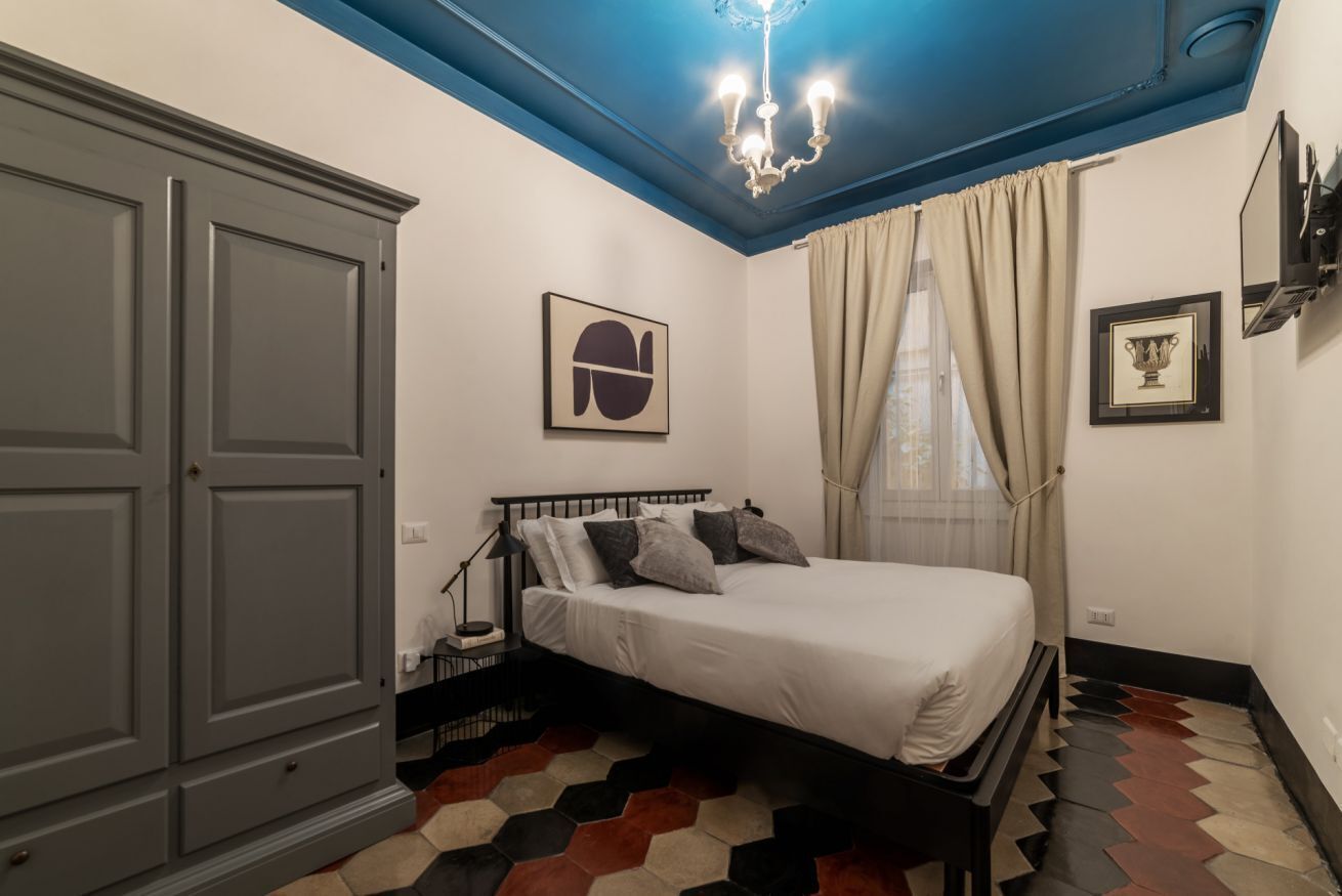 Une chambre à coucher avec un lit, une armoire, un lustre et une fenêtre avec des rideaux.