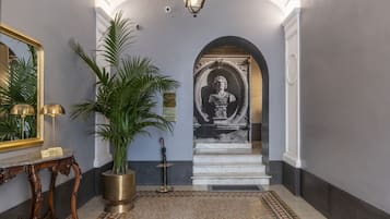 A grand hallway with a marble floor, a large potted plant, a mirror, and a statue at the end.