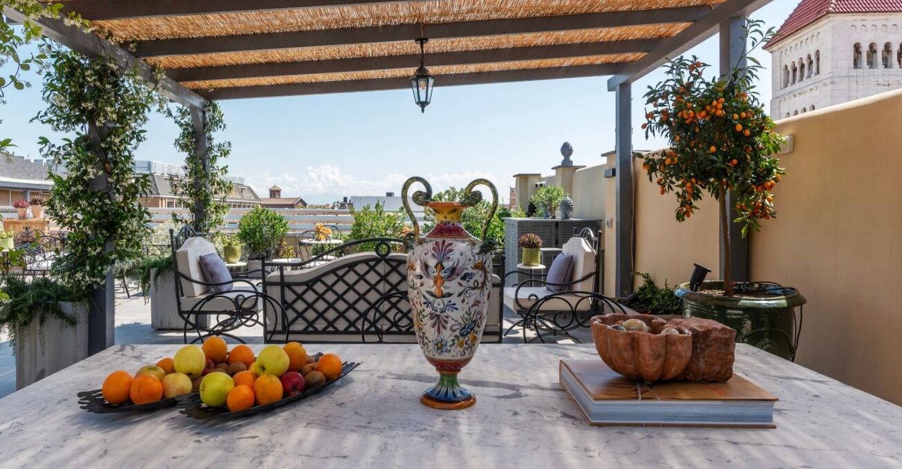 A terrace with a table set for dining, a decorative vase, and a view of the cityscape.