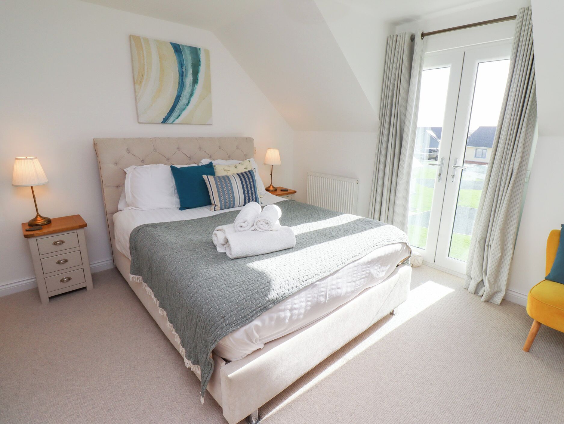 A neatly arranged bedroom with a bed, bedside tables, and a view of the outdoors through a sliding door.