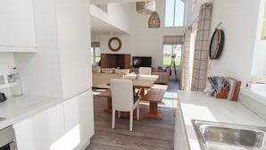 Una cocina moderna con armarios blancos, un comedor con mobiliario de madera y un ventanal que proporciona luz natural.