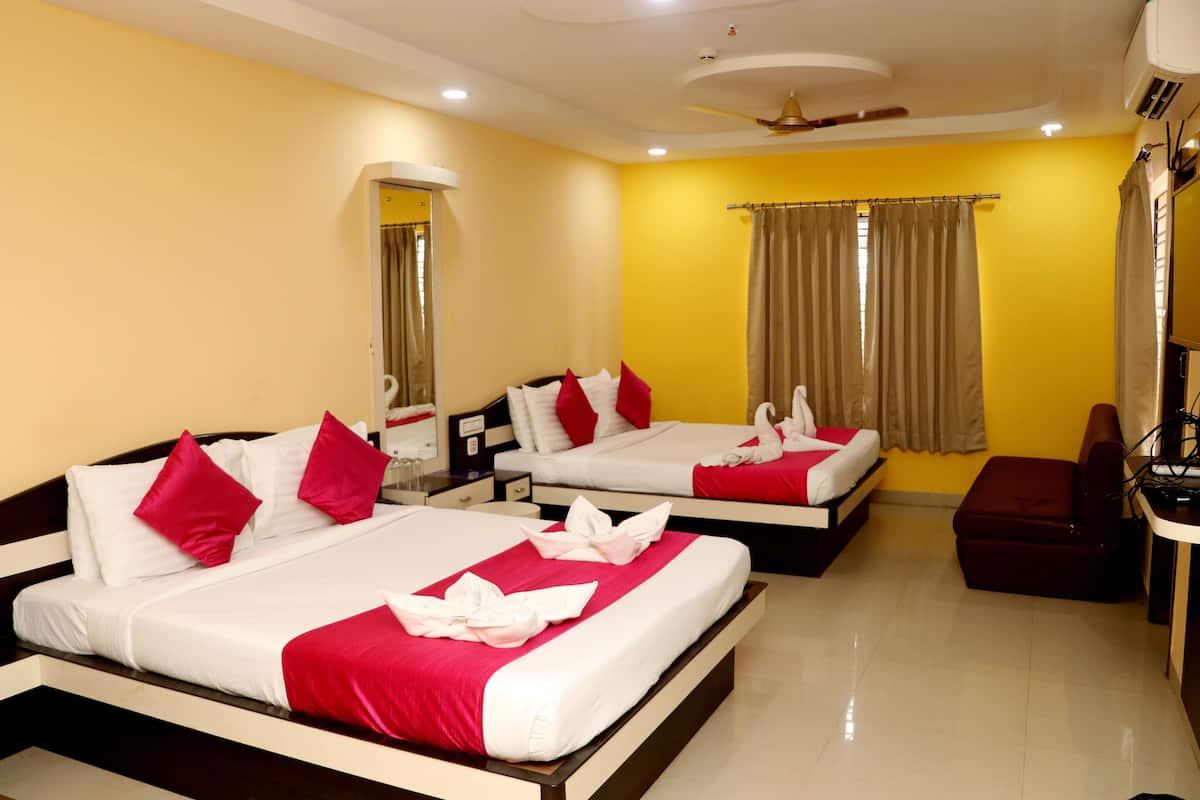 Une chambre d’hôtel avec deux lits, chacun agrémenté de draps rouges et blancs, un canapé marron, un bureau avec une chaise et un ventilateur de plafond.