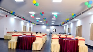 A conference room with rows of tables and chairs, decorated with colorful balloons. - Four Square Holidayz (Kanthi)