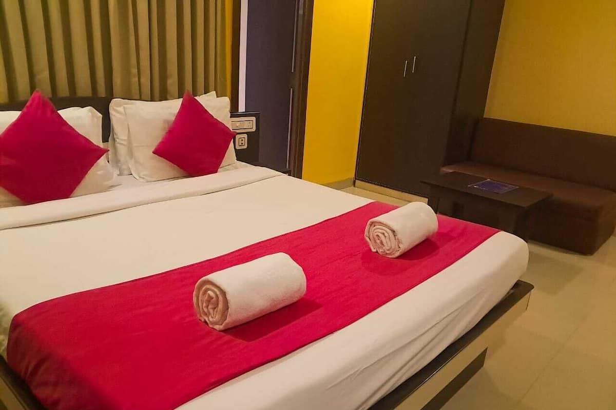 Une chambre d’hôtel avec un grand lit, deux oreillers, une couverture rouge et un banc marron.