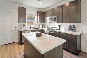 A modern kitchen with dark wood cabinets, a large island, stainless steel appliances, and a white countertop.