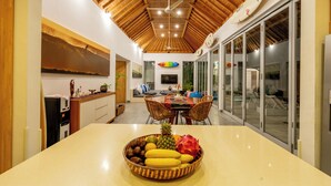 A modern kitchen with a wooden ceiling, a dining area with a table and chairs, and a fruit bowl on the counter. - Villa Becca Seminyak (Seminyak)