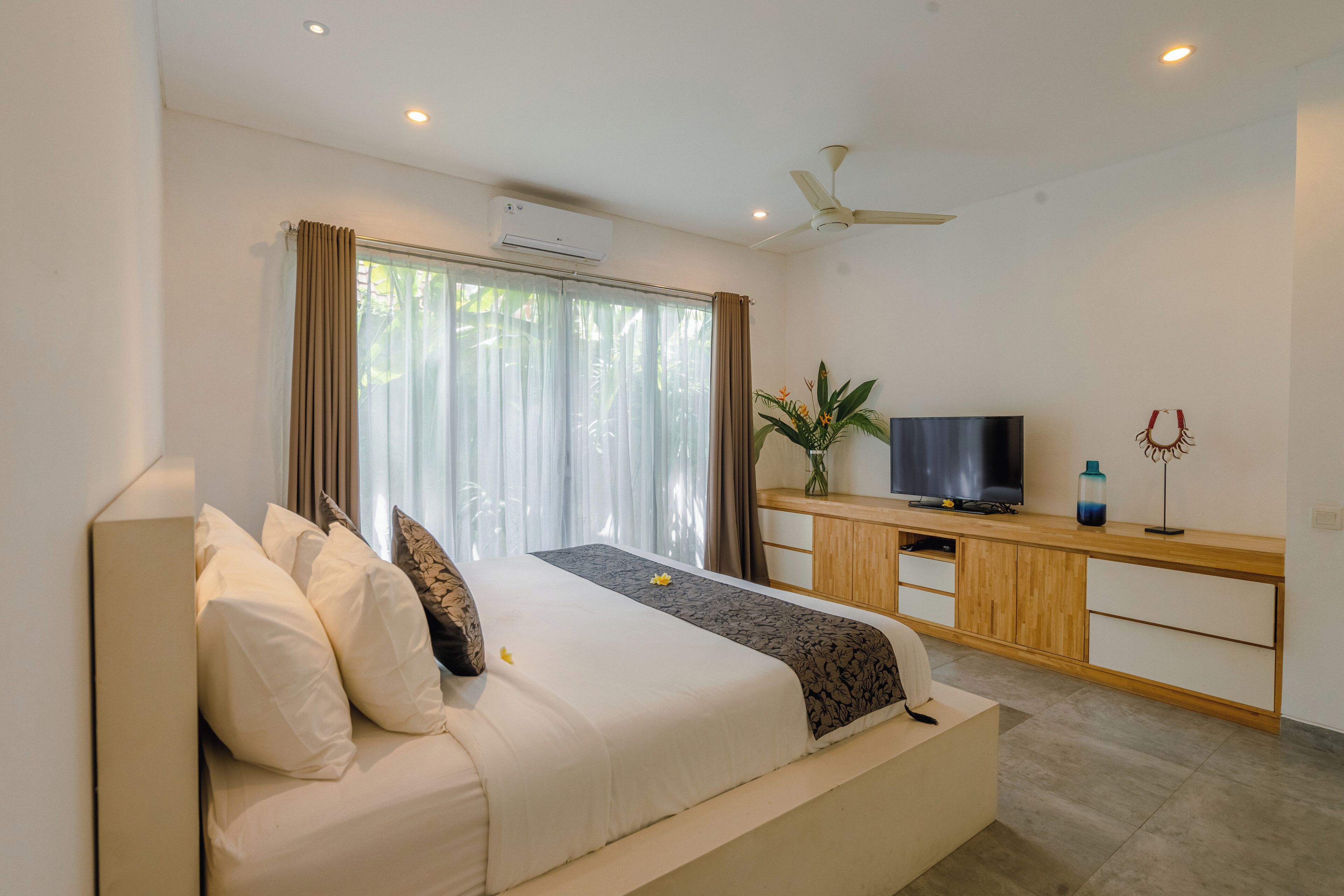 Un dormitorio moderno con cama, televisor, escritorio y ventilador de techo.
