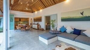 A spacious living area with a large sectional sofa, a dining table with chairs, a kitchen area, and a large painting on the wall. - Villa Becca Seminyak (Seminyak)