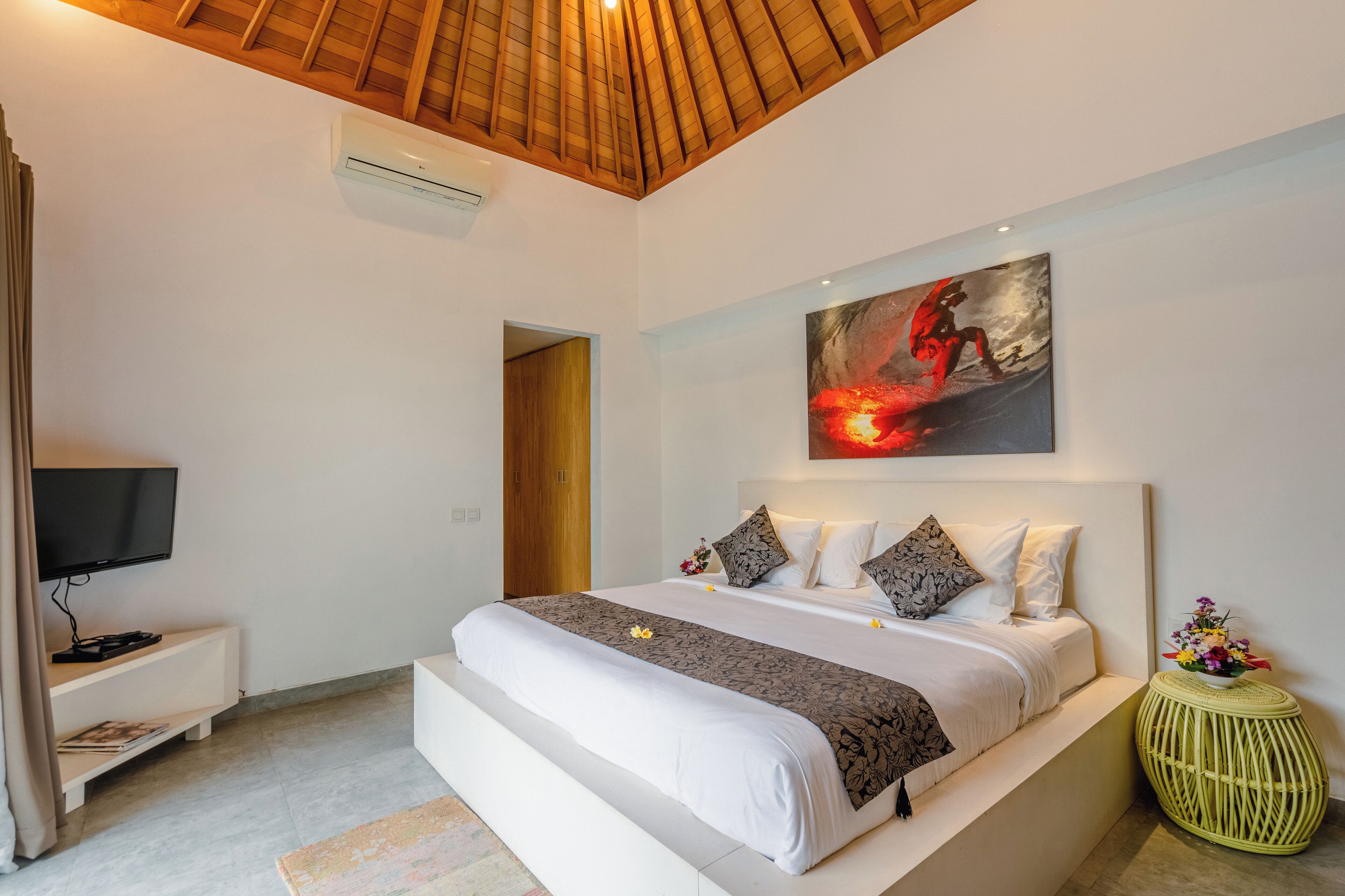 A modern bedroom with a large bed, a flat-screen TV, a painting, and a small side table.