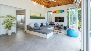 A modern living room with a large sectional sofa, a flat-screen TV, and a ceiling fan. - Villa Becca Seminyak (Seminyak)