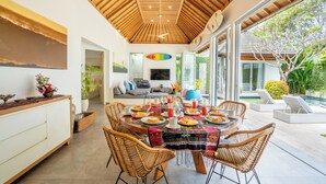 A dining area with a wooden ceiling, large windows, and a view of a swimming pool. - Villa Becca Seminyak (Seminyak)
