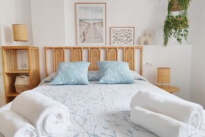 Ein ordentlich eingerichtetes Schlafzimmer mit Bett, Kissen, Nachttisch, Lampe, einer Ablage mit Korb und Wandbildern.