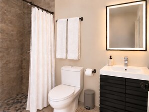 A bathroom with a toilet, a sink, a mirror, a shower curtain, and a trash bin.