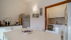 Une cuisine moderne avec des meubles blancs, un réfrigérateur en acier inoxydable, un four encastré et un four à micro-ondes. On y trouve une table à manger avec un saladier, ainsi qu’une machine à café posée sur le plan de travail.