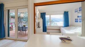 Une pièce comprenant un lit, une table à manger avec des chaises, un meuble blanc et une vue sur l’extérieur grâce à une porte-fenêtre coulissante.