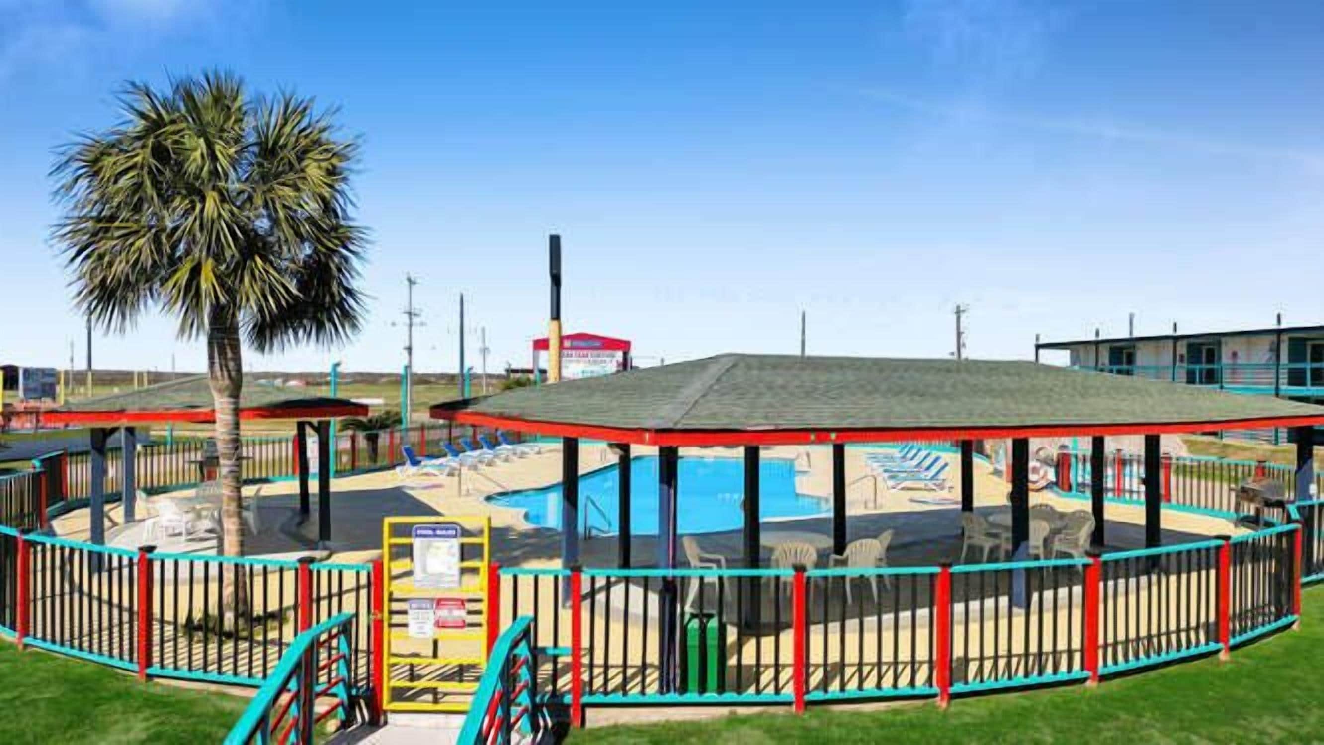A pool area with a fenced deck, a covered seating area, and a palm tree.