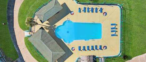 An aerial view of a resort with a swimming pool, sun loungers, and a fenced area.
