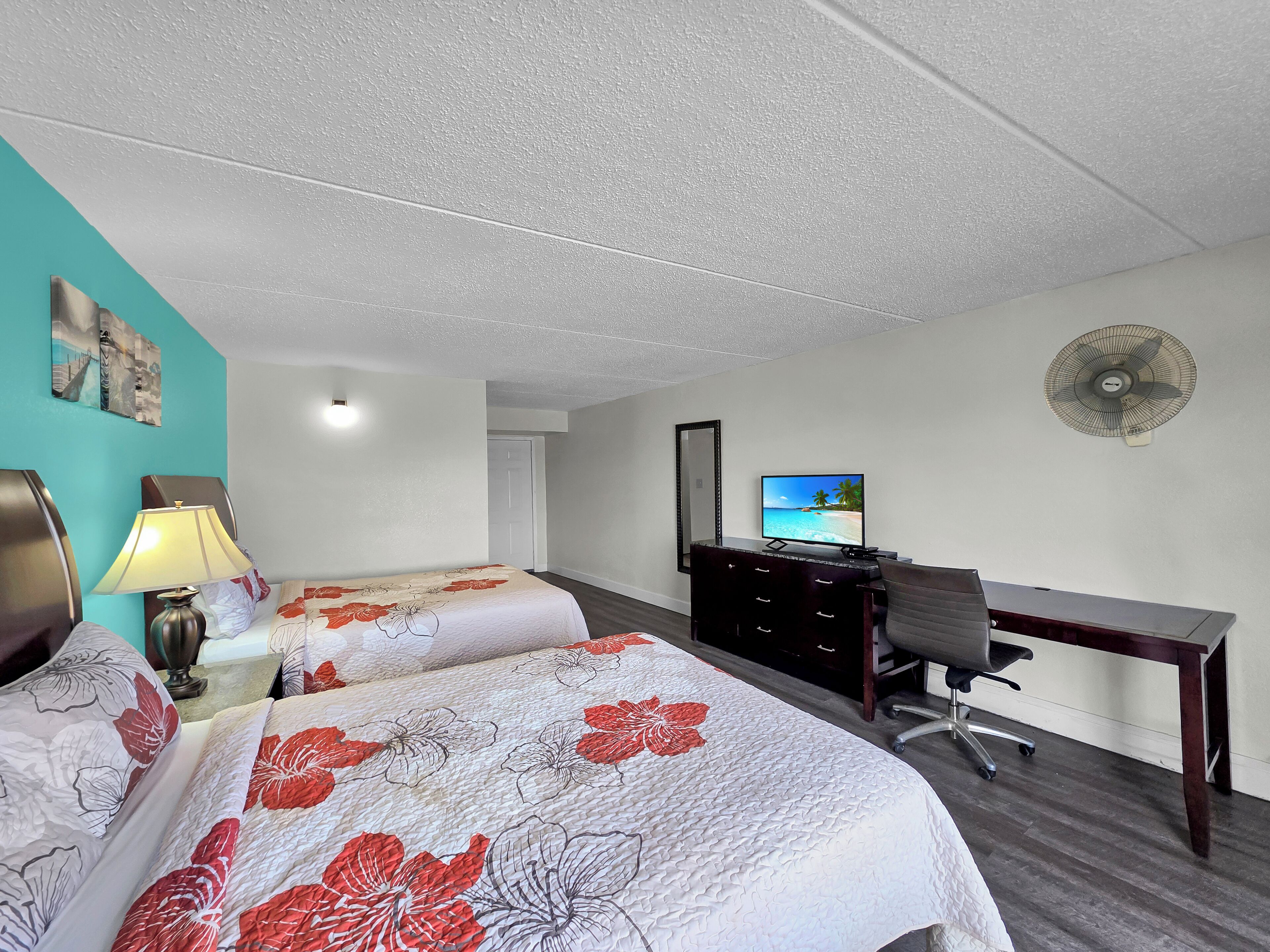 Habitación de hotel con dos camas, un escritorio, una silla, un televisor y un ventilador de pared.