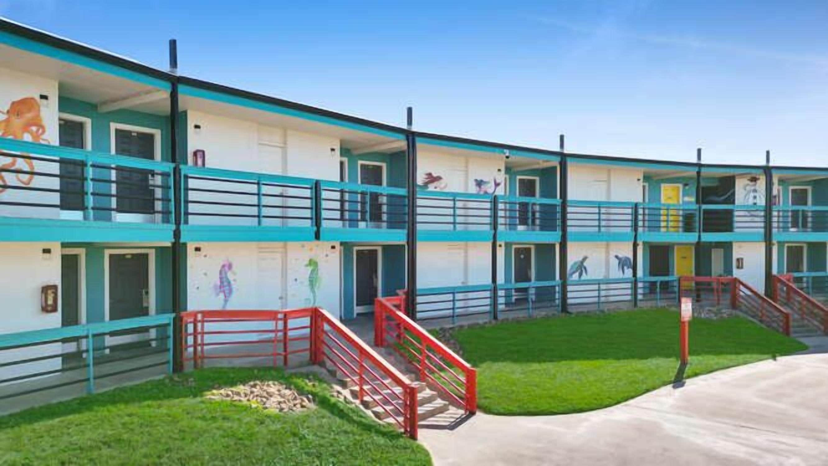 A multi-story motel with a flat roof, a central courtyard, and a red railing around the perimeter.