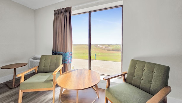 A room with two green upholstered chairs, a wooden table, and a large window with a view of a grassy field. - Crystal Palace Resort (Port Bolivar)