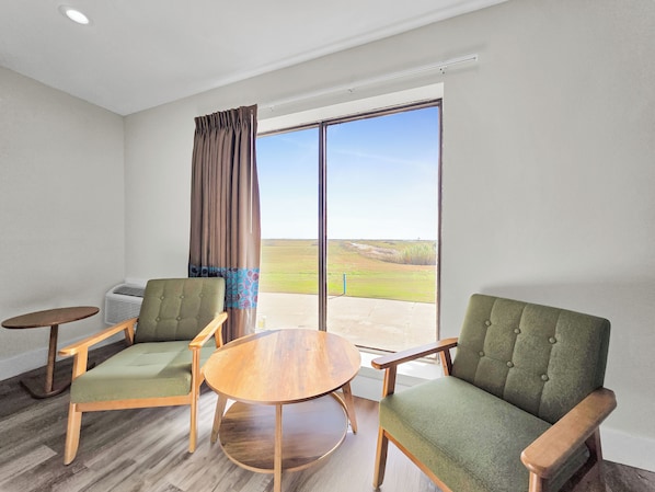 A room with two green upholstered chairs, a wooden table, and a large window with a view of a grassy field. - Crystal Palace Resort (Port Bolivar)