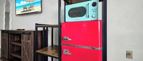 Una cocina con un refrigerador rojo, una mesa de madera y un ventilador fijado a la pared.