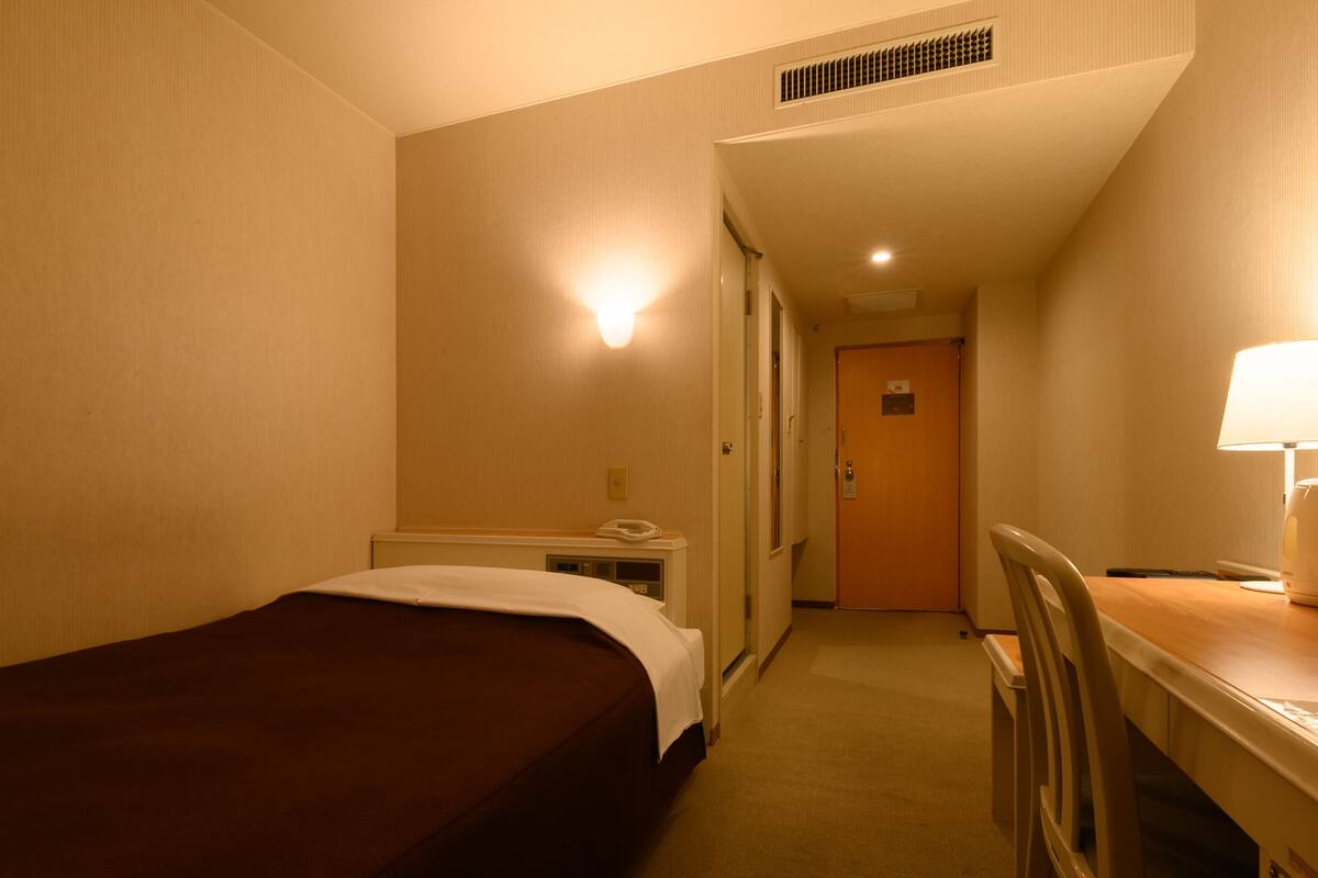 Una habitación de hotel con una cama individual, un escritorio con lámpara, una silla y un teléfono.