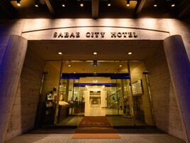 L’entrée de l’hôtel Sabae City se distingue par sa façade en verre, un comptoir d’accueil et un escalier menant à l’intérieur.