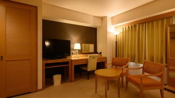A hotel room with a desk, television, lamp, and two chairs.