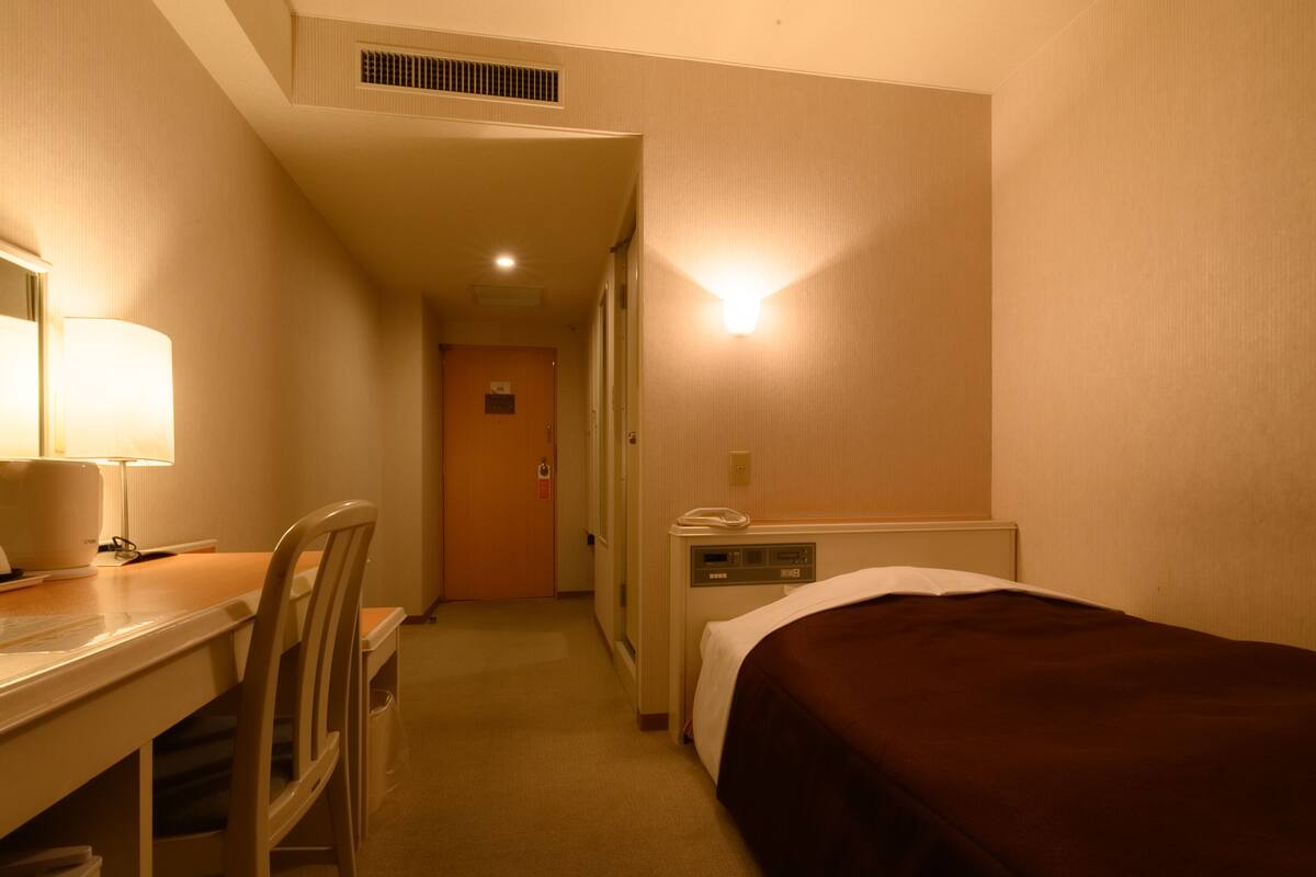 Una habitación de hotel con escritorio, silla, cama y teléfono en una mesita de noche.