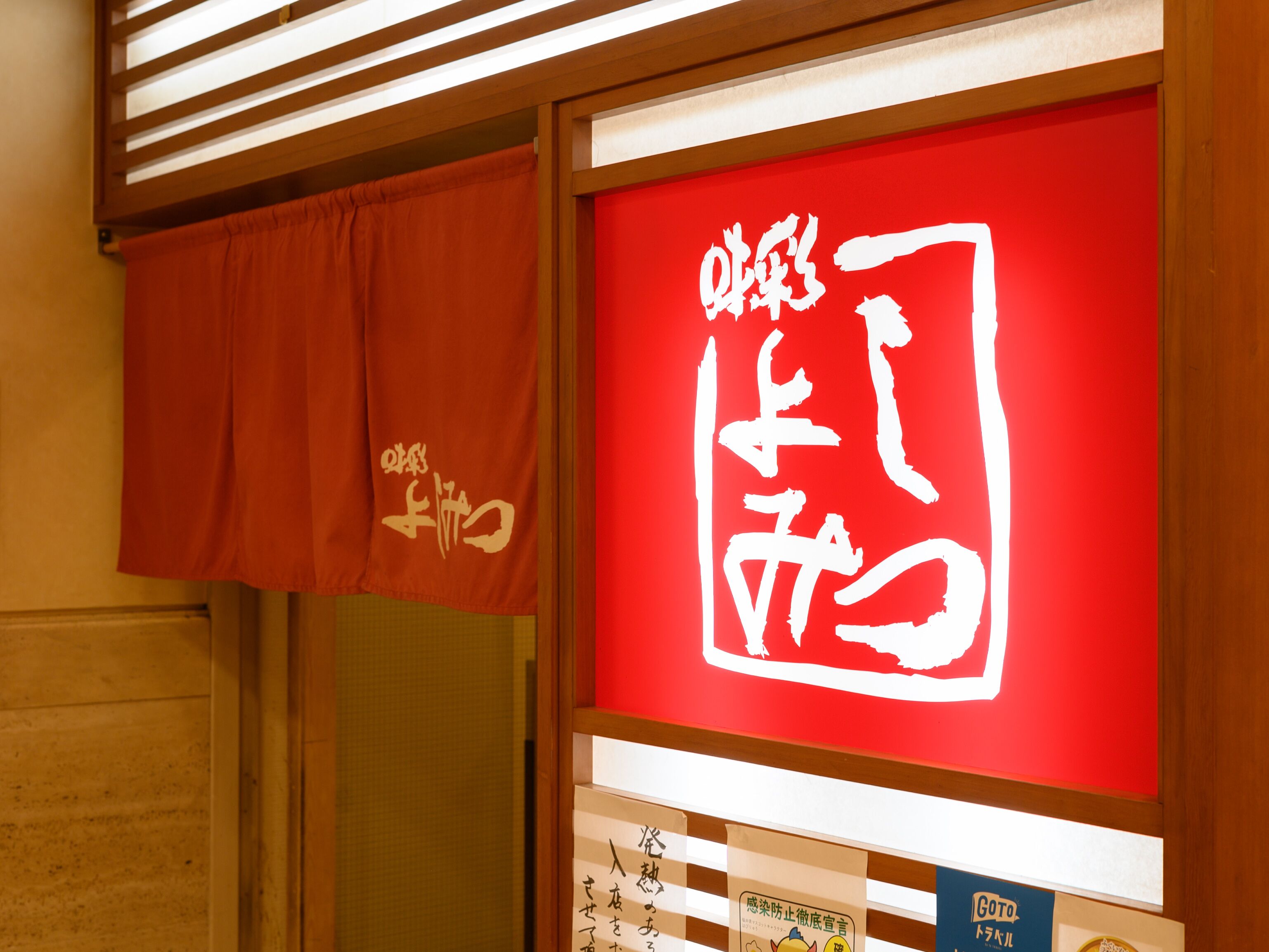 A red sign with white Japanese characters, a wooden slatted ceiling, and a brown curtain with white text.