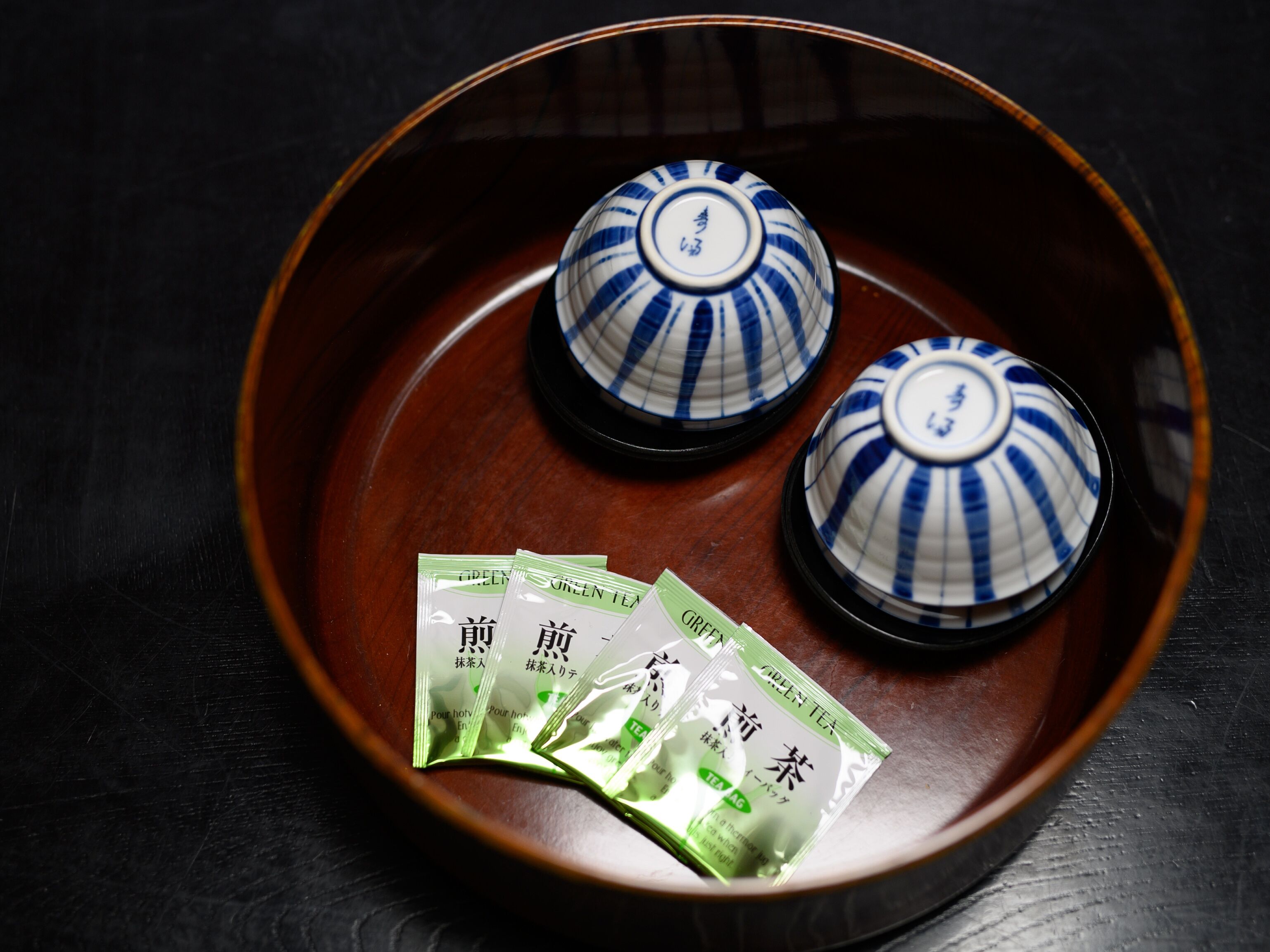 A traditional Japanese tea set with two ceramic cups and three green tea packets on a wooden tray.