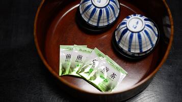 A traditional Japanese tea set with two ceramic cups and three green tea packets on a wooden tray.