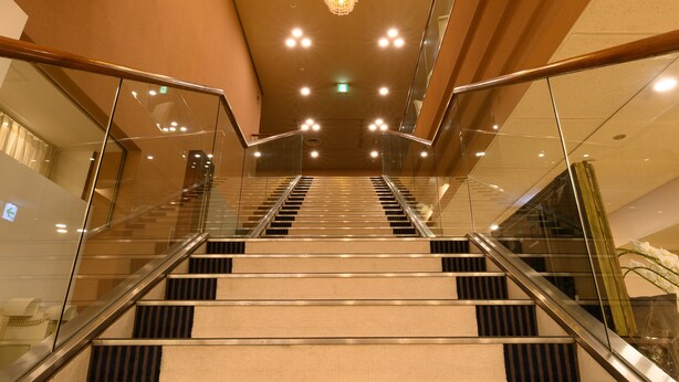 A modern hotel interior with a glass staircase, wooden paneling, and a chandelier. - Sabae City Hotel (Sabae)