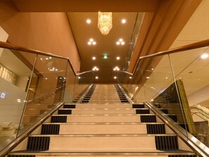 Un intérieur d’hôtel moderne avec un escalier en verre, des lambris en bois et un lustre.