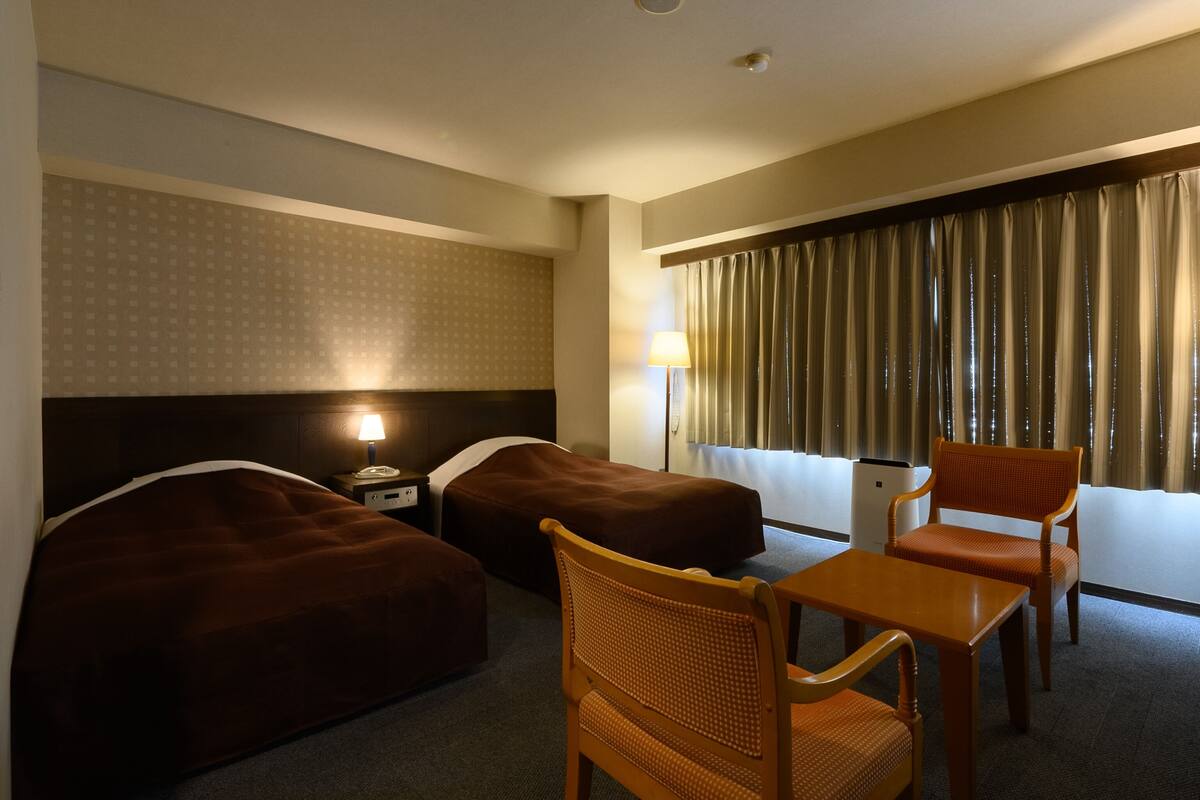 Habitación de hotel con dos camas, una mesita y una silla.