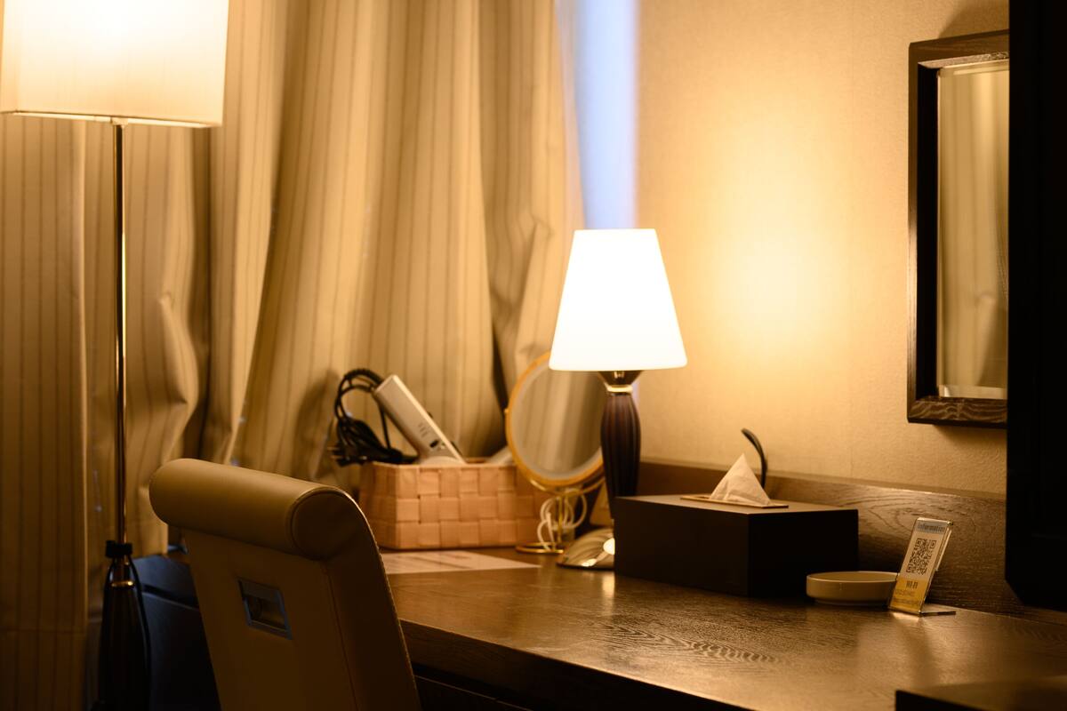 Habitación de hotel con escritorio, lámpara, silla, cesta, caja de pañuelos y espejo.