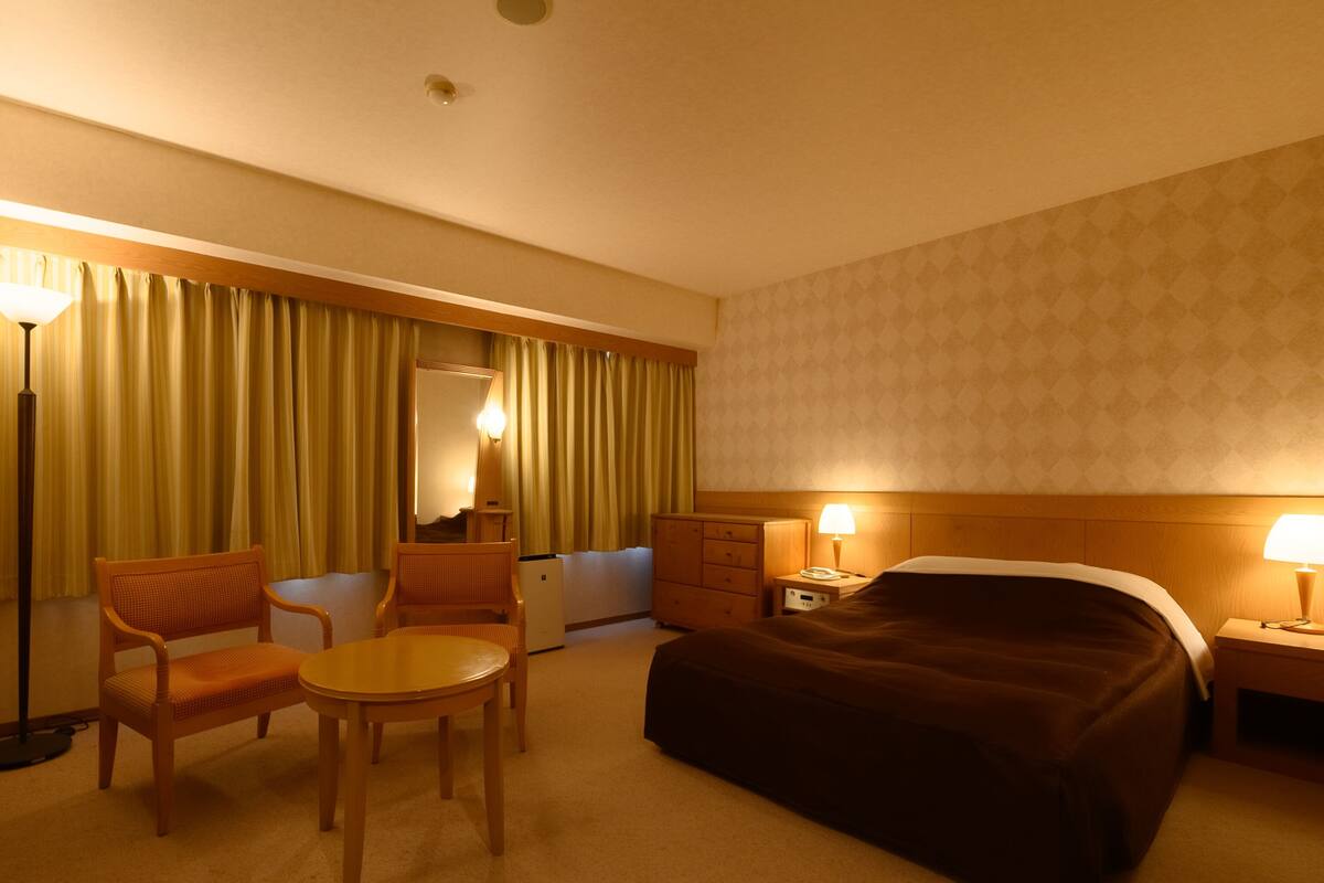 Habitación de hotel con cama, escritorio, silla, lámpara y cómoda.