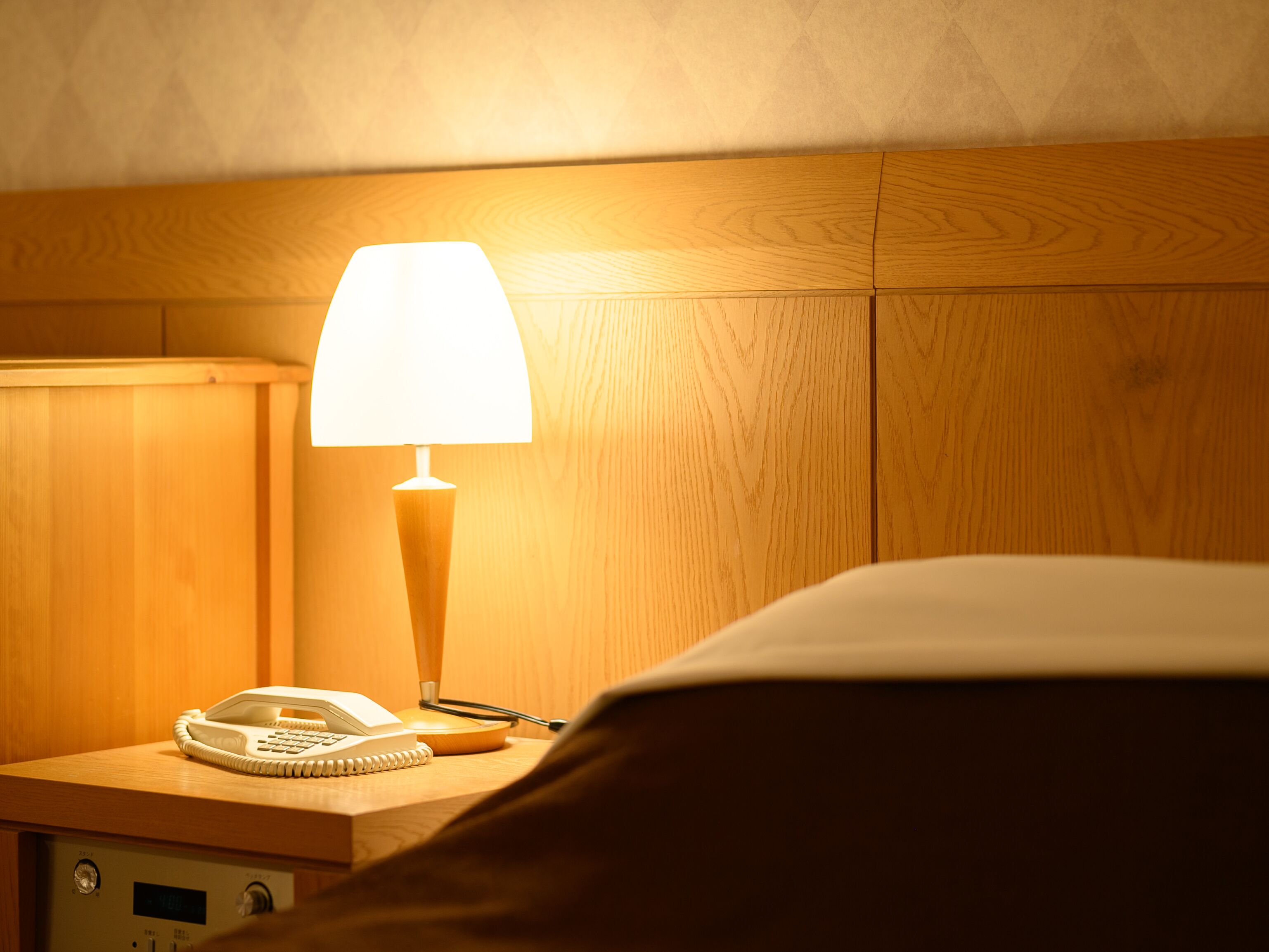 A wooden bedside table with a lamp, a telephone, and a notepad.