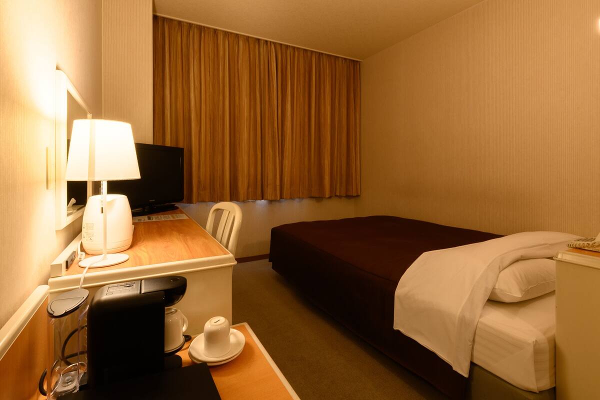 Una habitación de hotel con una cama, un escritorio con lámpara, cafetera y televisor.