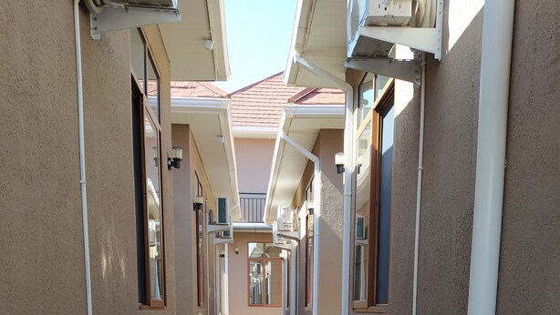 A corridor with tiled flooring, walls with external pipes, and windows with blinds. - Hancol Hotel (Dodoma)