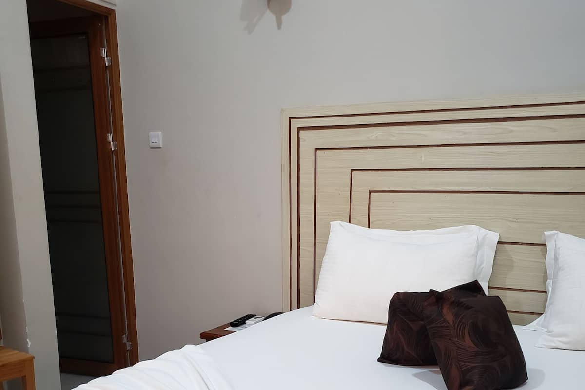 A neatly made bed with white linens and two decorative pillows, a wooden headboard, and a wall-mounted light fixture.