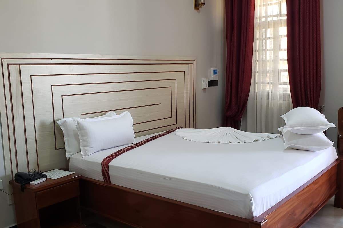 A hotel room with a large bed, a nightstand, a telephone, and a wall-mounted air conditioning unit.