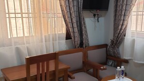 A room with a wooden sofa, a wooden table, and a small round table with two bottles on it. - Hancol Hotel (Dodoma)